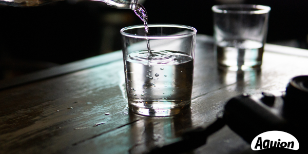 Glasflasche mit Wasser füllt ein Glas - AQUION ist Teil des Refill-Netzwerks