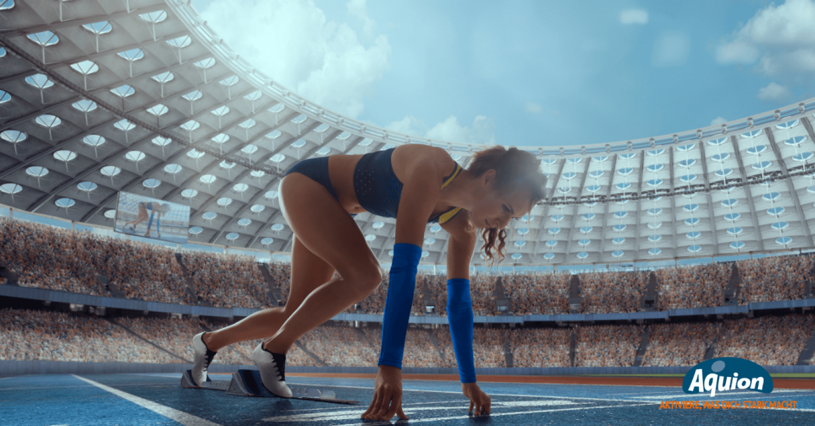 Eine Läuferin in einem blauen Laufset ist in einem voll besetzten Sportstadion und befindet sich in der Startposition, um mit dem Rennen zu beginnen. Sie hat sich auf ihren Fingern abgestützt und die Füße auf die Starthilfe gestellt.